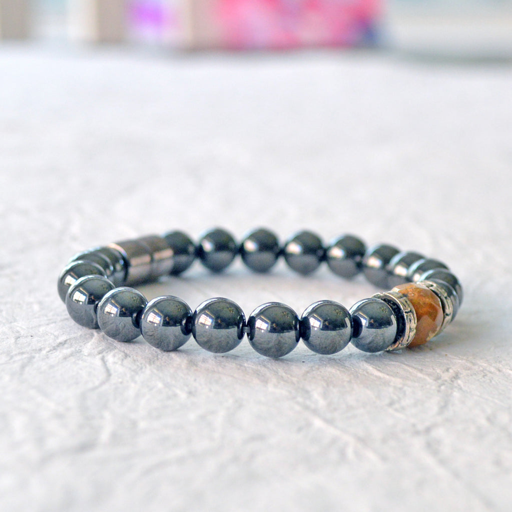 Magnetic bracelet handcrafted with black high power magnetic hematite beads. In the center is a single wood fossil bead surrounded by Tibetan silver bead caps.